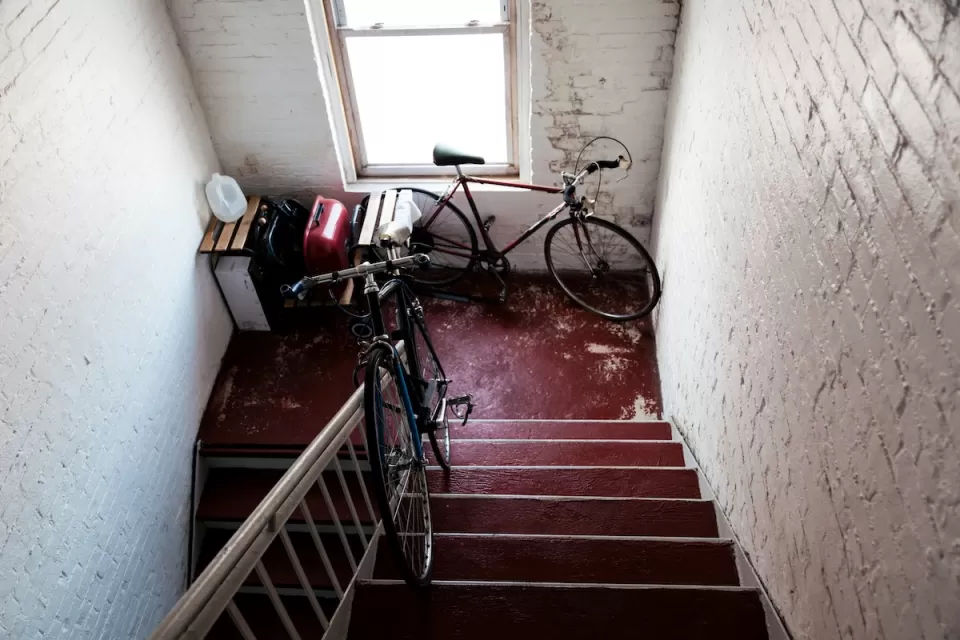 Two bicycles in apartment building stairwell landing with white painted brick walls.